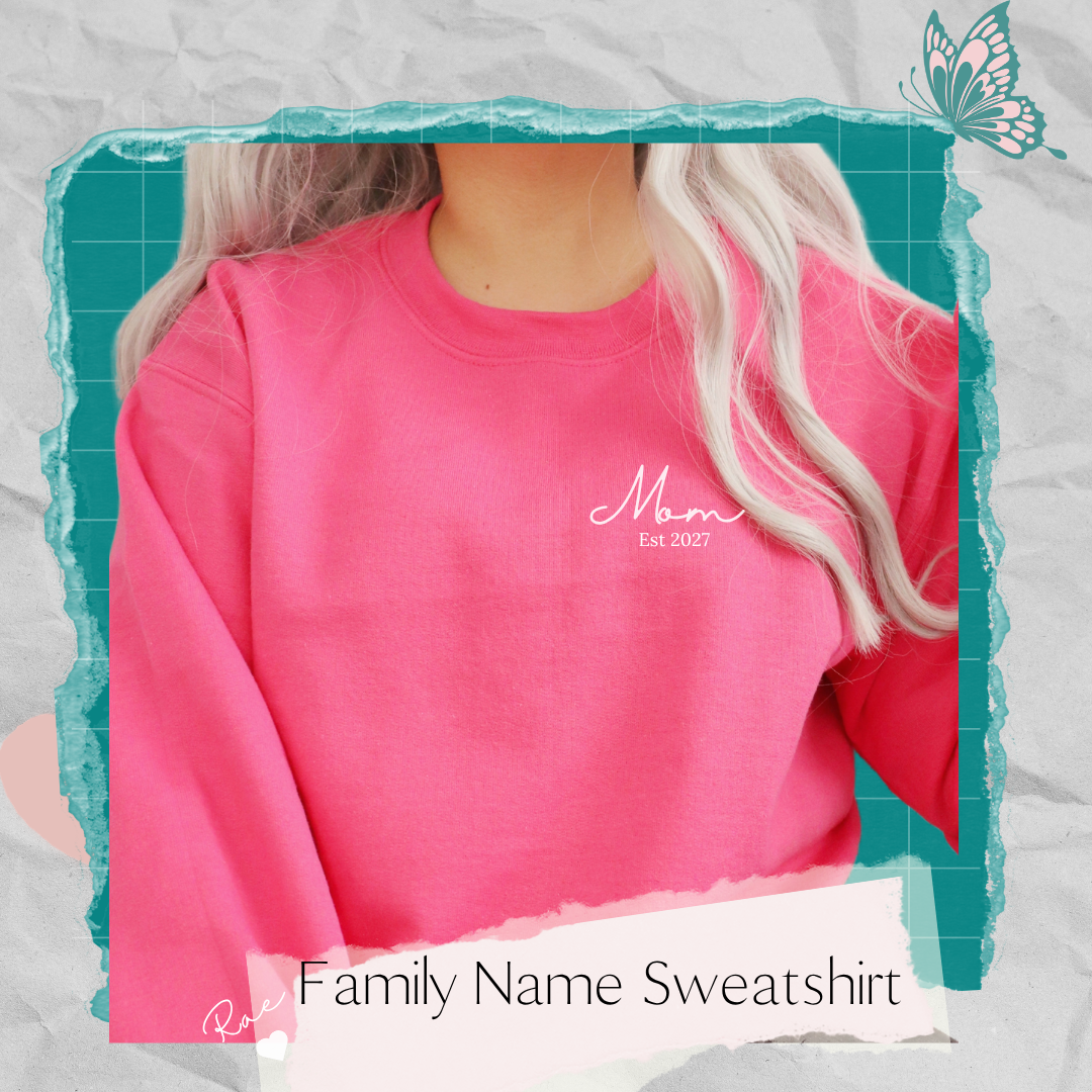 Pink sweatshirt with white “Mom Est 2027” on the front left chest and “Rae” with a heart on the right sleeve.